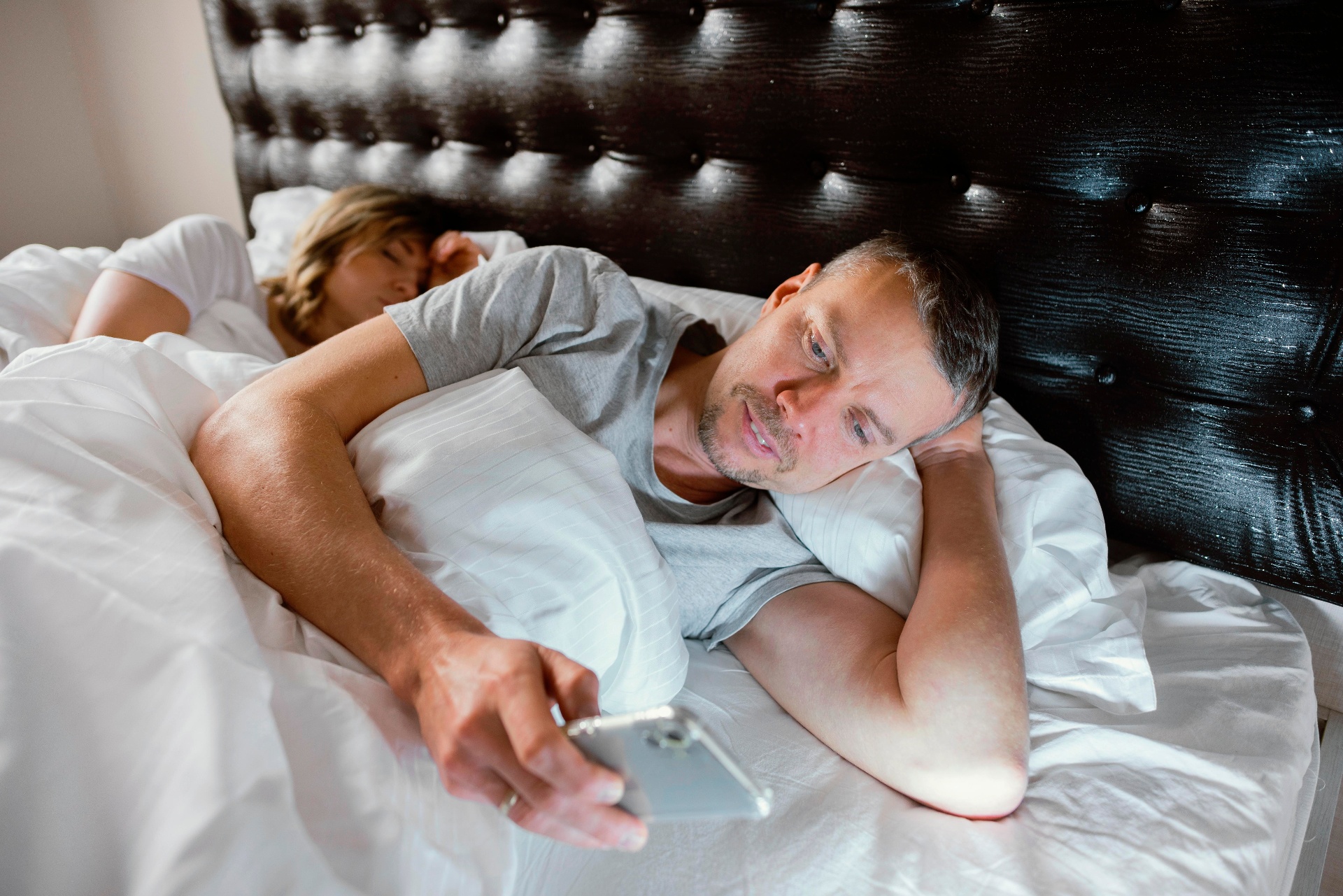 Persona sveglia di notte con lo smartphone mentre il partner dorme